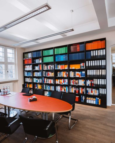 Gruneberg Rechtsanwälte Besprechungsraum mit großer Bücherwand und einem großen ovalen Tisch mit Stühlen.