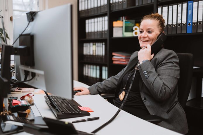 Eine Frau im Büro telefoniert und arbeitet am Computer.