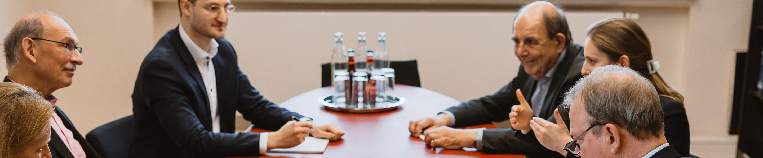 Mehrere Personen sitzen um einen Konferenztisch und diskutieren miteinander.